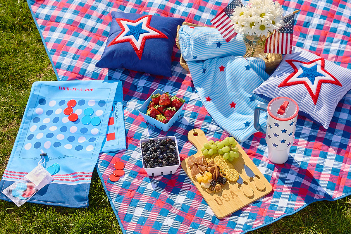 A photo of Dollar General's patriotic decor and entertaining including picnic blanket, game, throw, pillows, centerpiece, berry holders, fresh fruit, charcuterie board and tumbler.